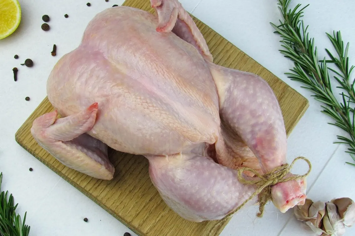 Gà nguyên con làm sạch lông trên thớt gỗ sáng màu