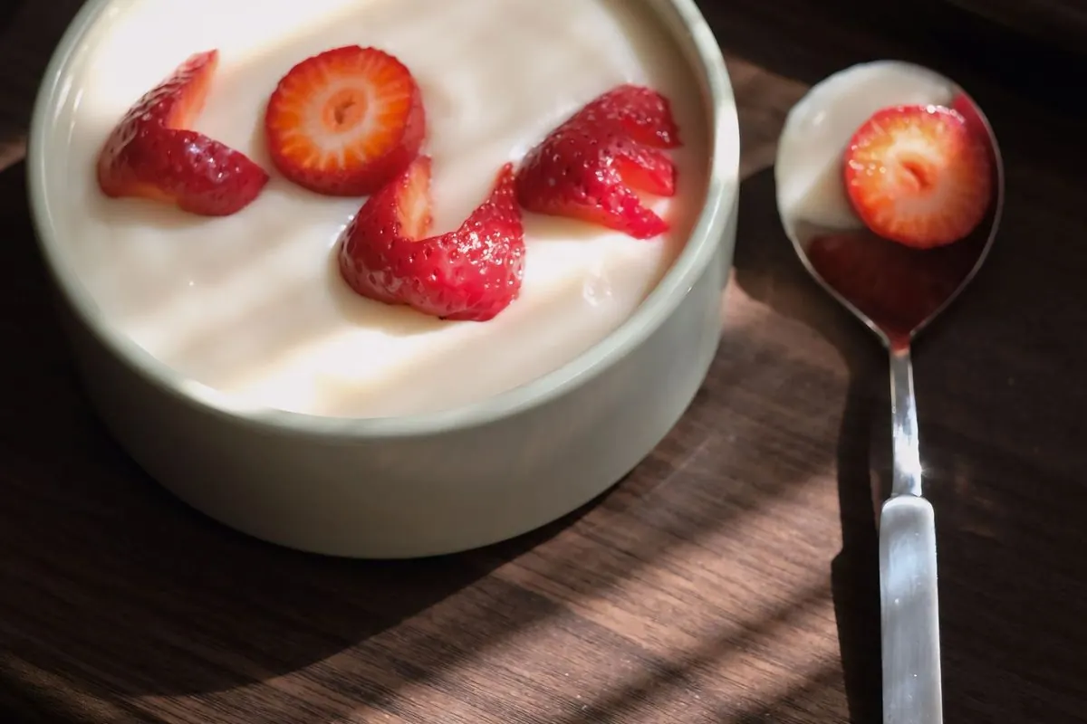 Bowl of white yogurt with strawberry slices and a spoon