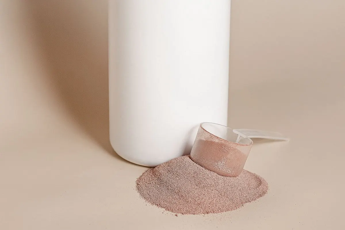 Hộp nhựa trắng và muỗng đong đầy bột whey