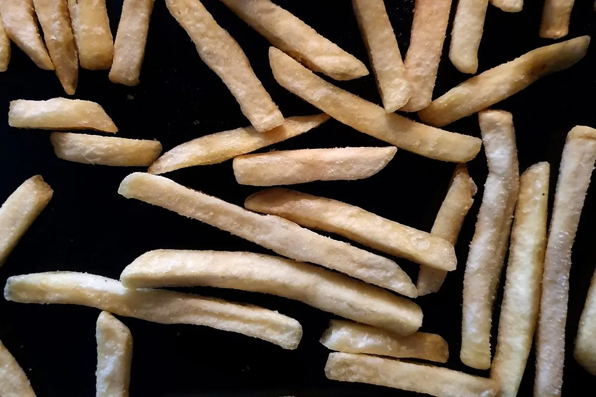 Uncooked cut potato fries scattered on a black tray