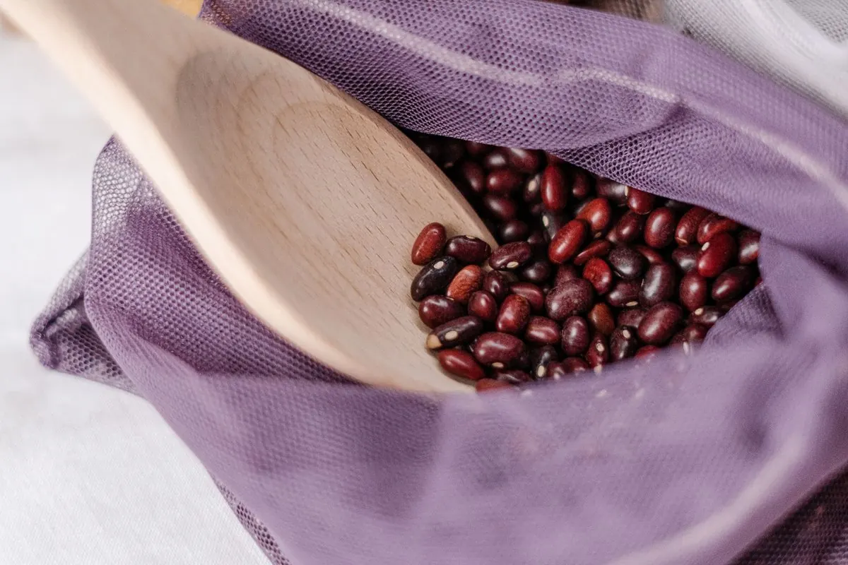 Dried adzuki beans in a net bag with a wooden scoop