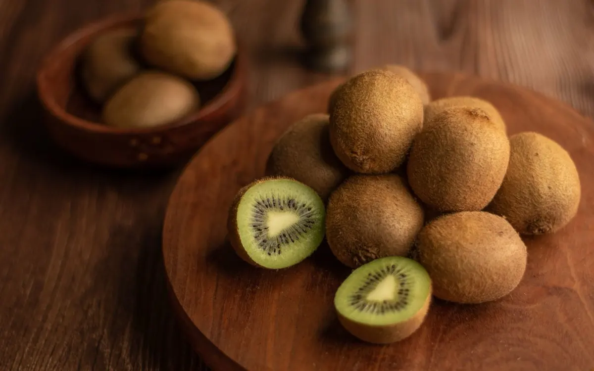 Quả kiwi nguyên trái và bổ đôi trên đĩa gỗ