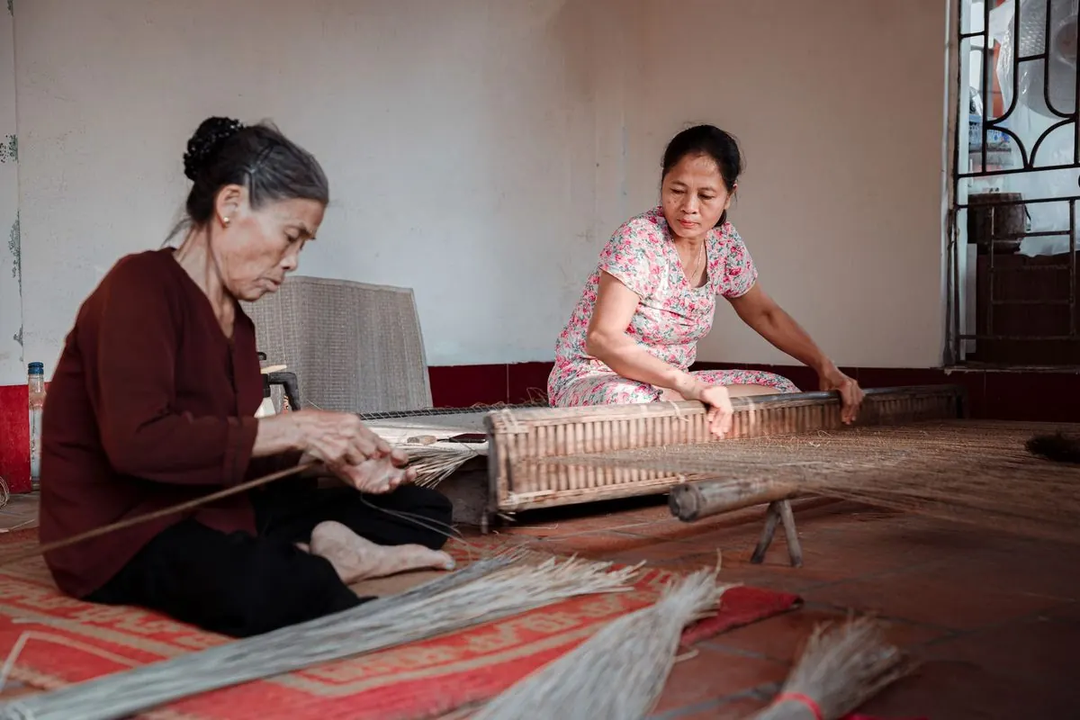 Hai phụ nữ ngồi dệt chiếu từ sợi cói trong nhà