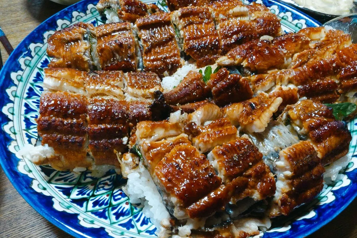 Kabayaki grilled eel pieces on rice on a blue ceramic platter