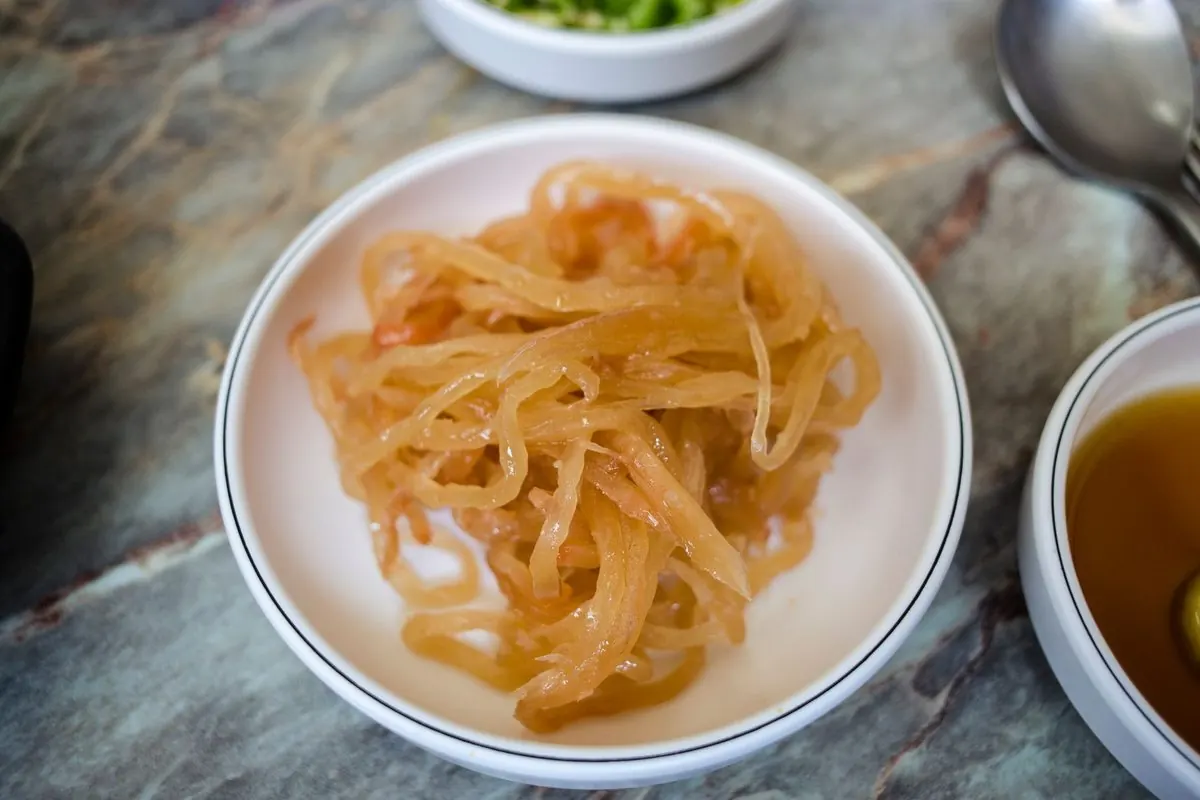 Shredded golden-brown jellyfish in a white porcelain dish