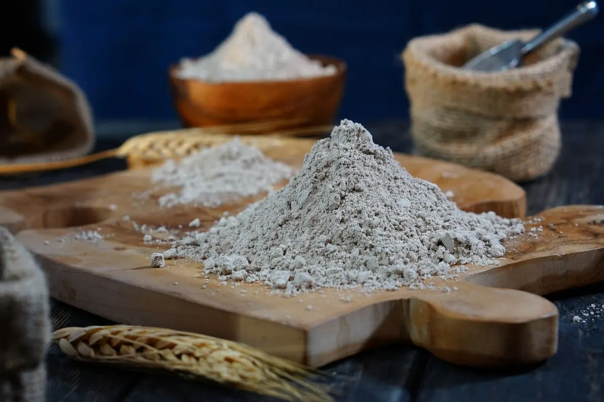 Đống bột mì trên thớt gỗ cạnh bao bố và bông lúa mì