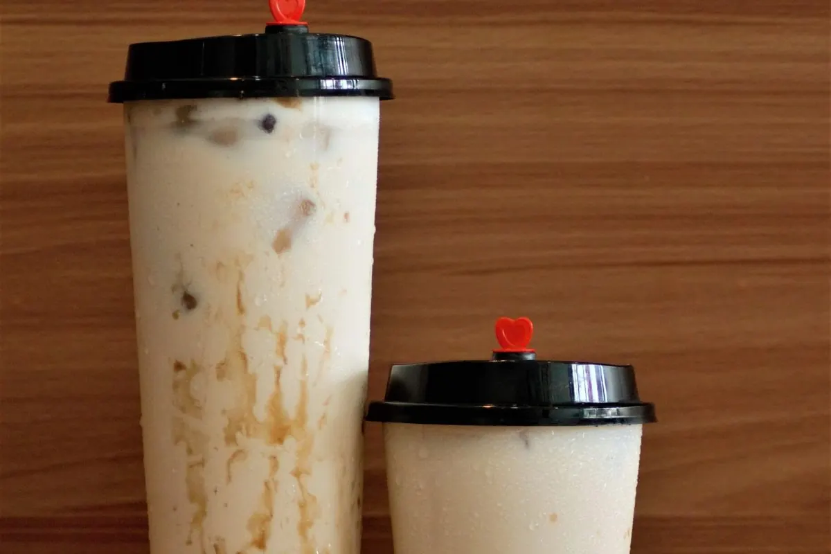 Two tall cups of milk tea with black tapioca pearls at the bottom