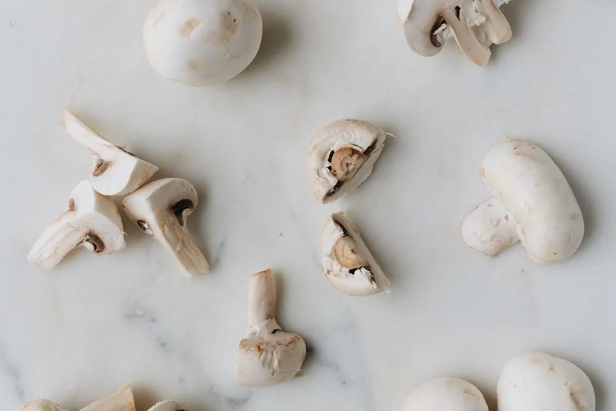 Whole and sliced white button mushrooms on a marble surface