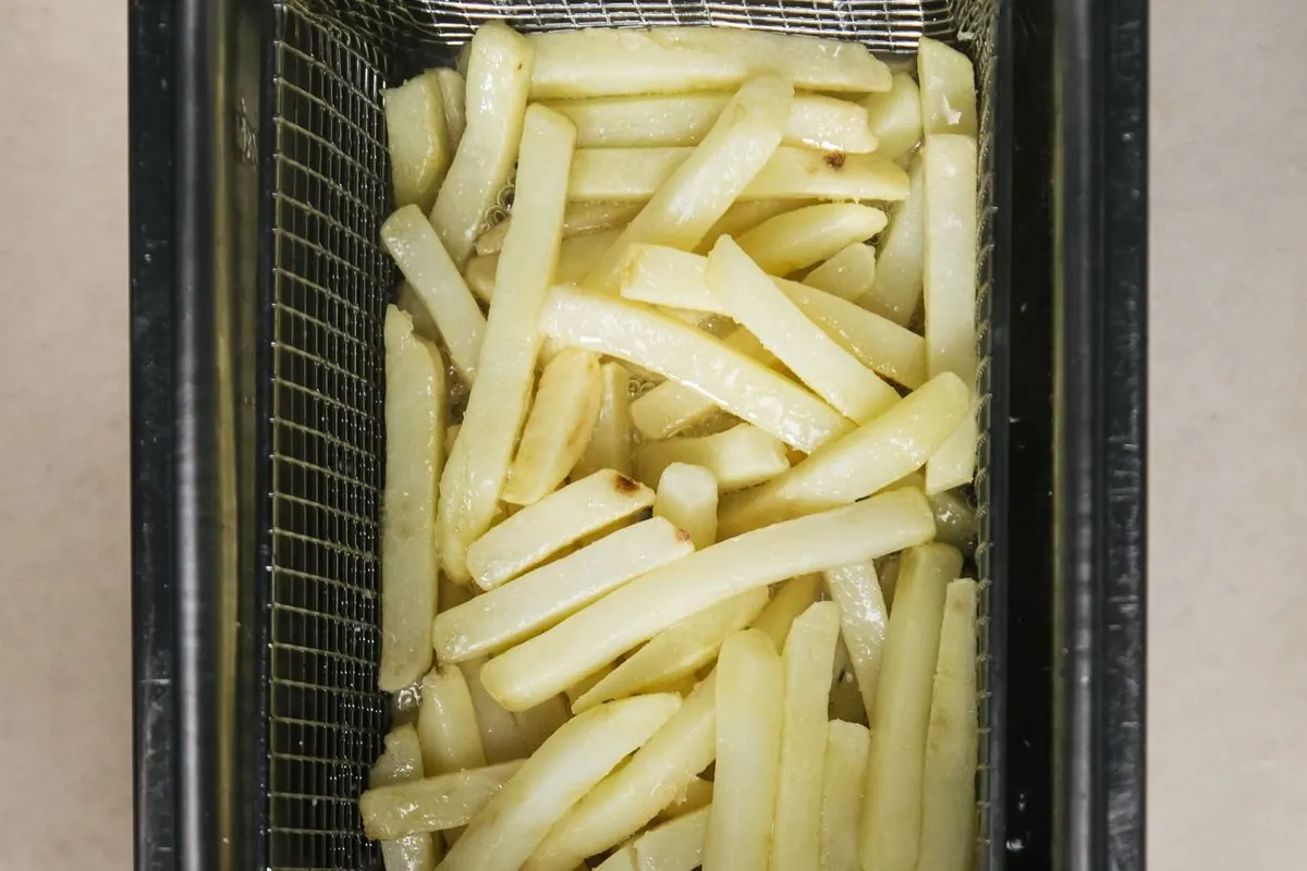 Pre-cut potato fries in a stainless steel fryer basket