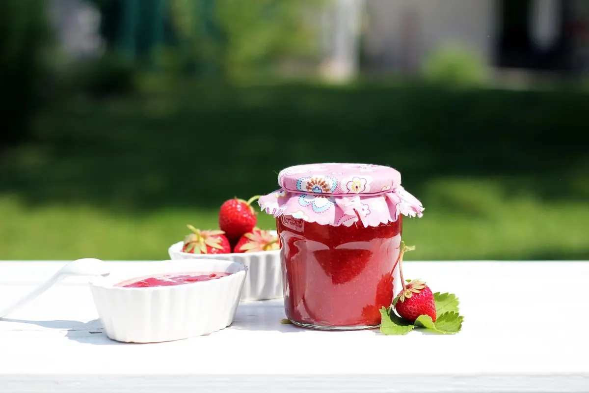 Jar of strawberry jam beside a dish of jam and fresh strawberries