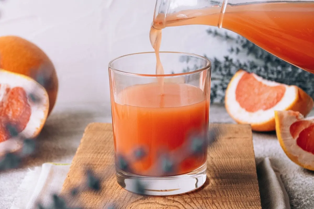 Rót nước ép bưởi hồng vào ly, cạnh bưởi bổ đôi