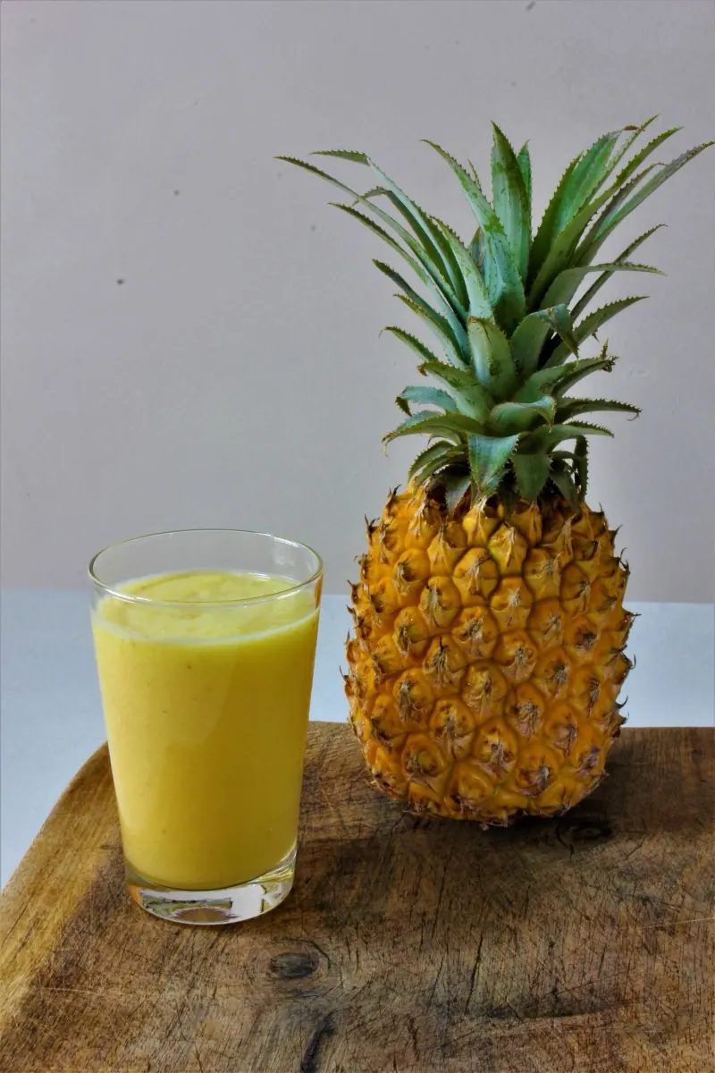 Glass of pineapple juice beside a fresh pineapple