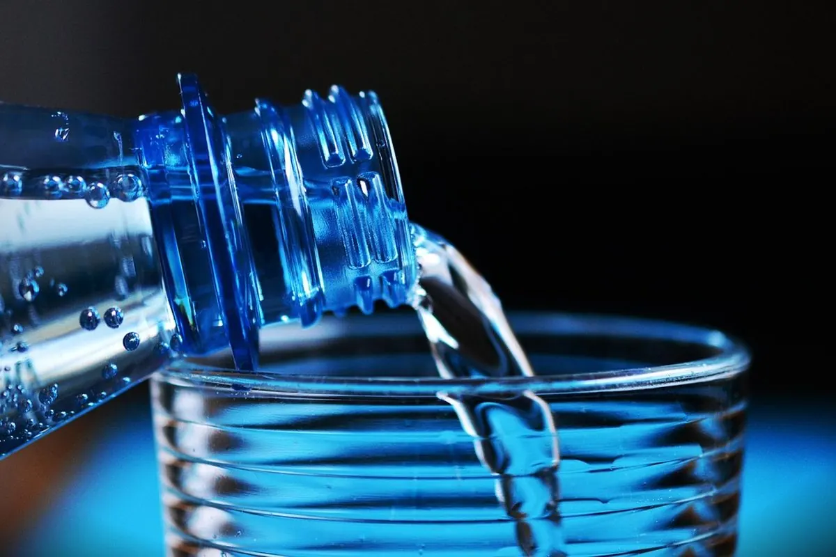 A water bottle tilted to pour into a glass, blue backdrop