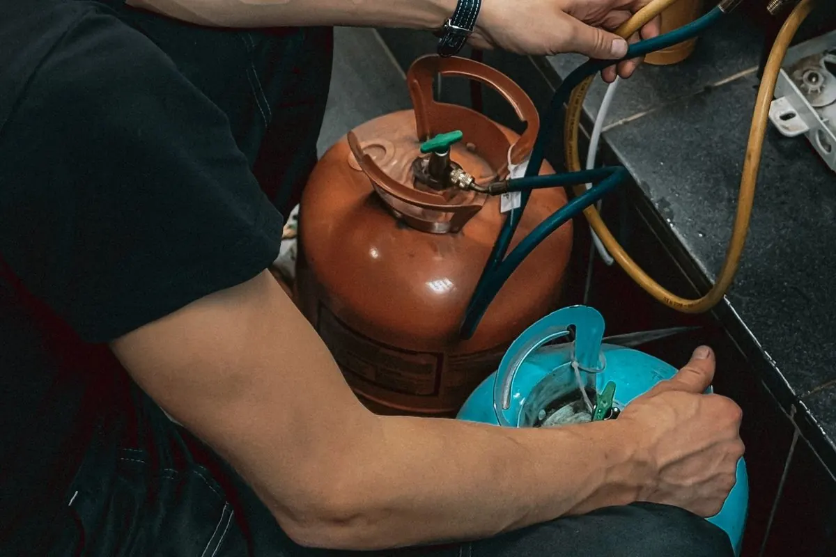 Thợ điện lạnh nối ống nạp từ hai bình gas lạnh màu cam và xanh