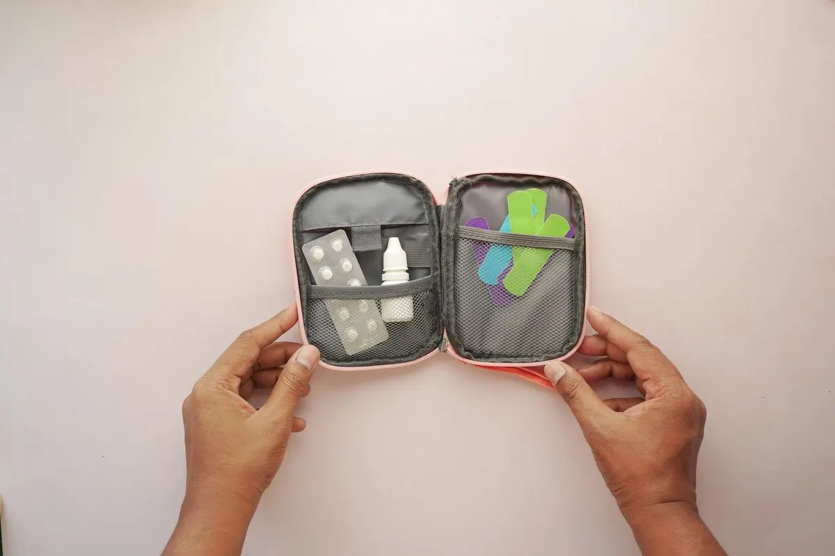 Hai tay mở túi sơ cứu có băng dán, vỉ thuốc và lọ nhỏ