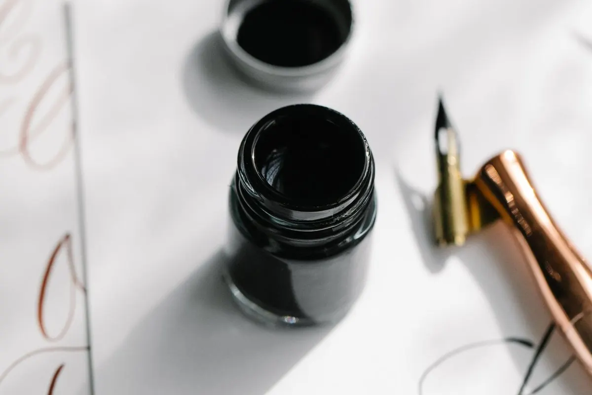 Bottle of black writing ink beside a dip pen nib