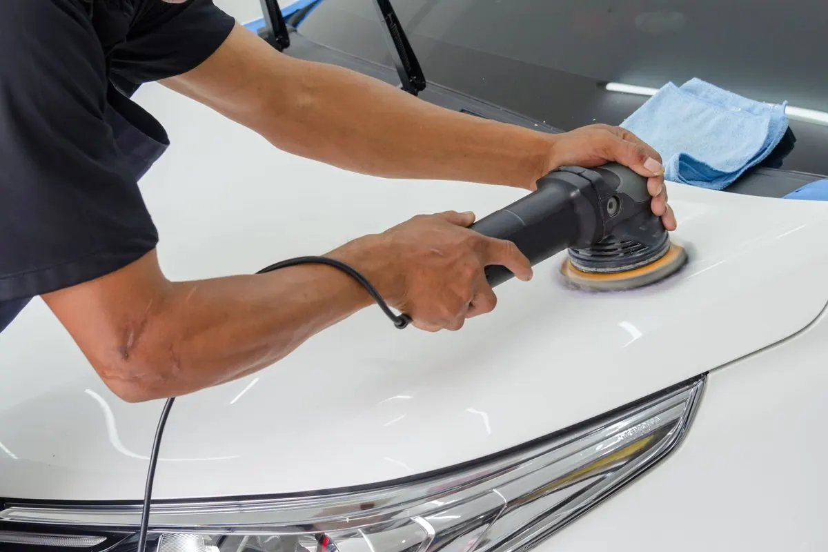 Worker polishing the bodywork of a white car with a machine polisher