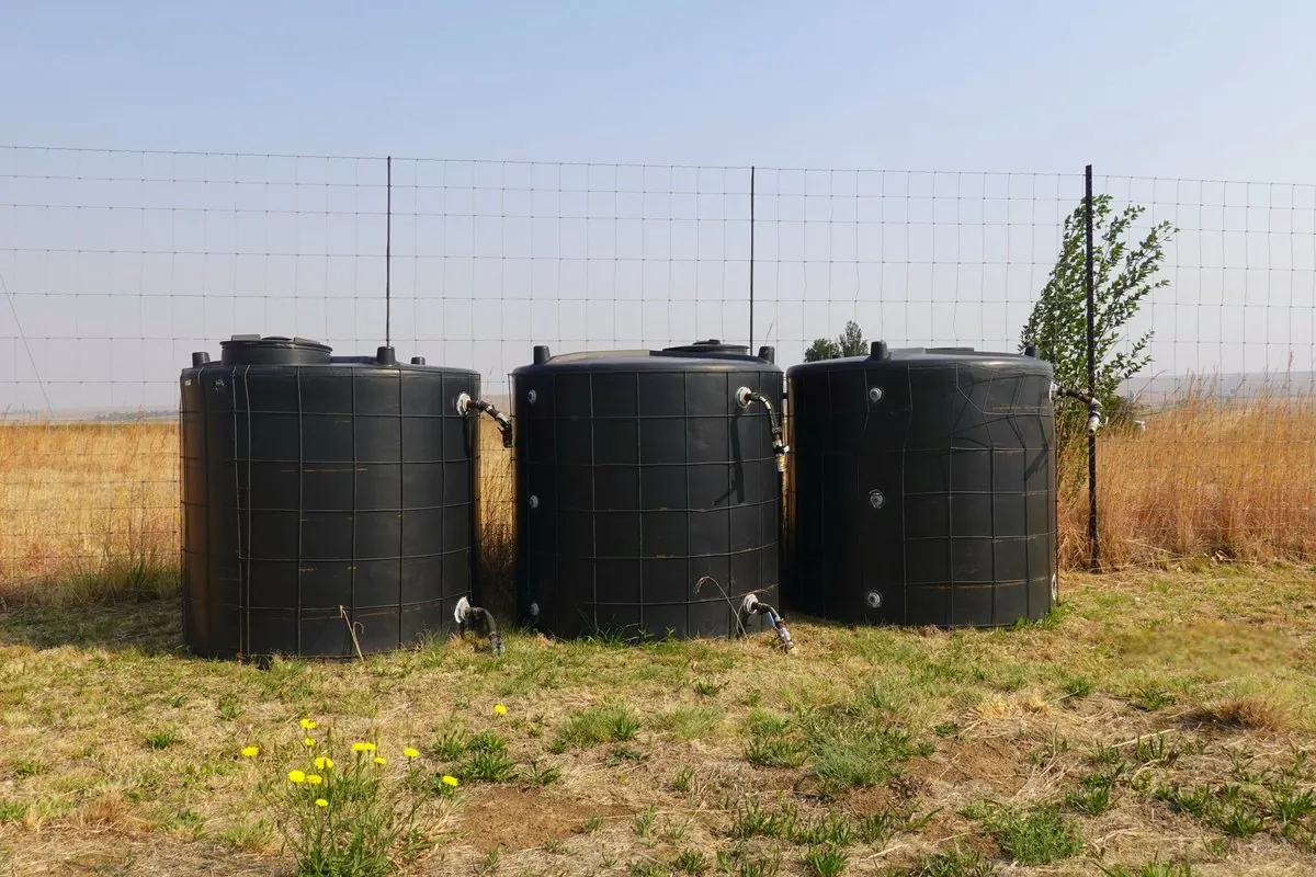 Three large black plastic water storage tanks standing on a grassy field