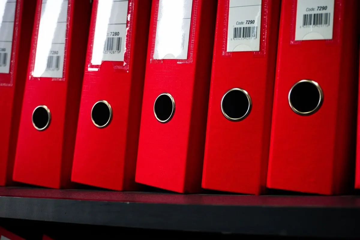 A row of red lever arch binders on an office shelf