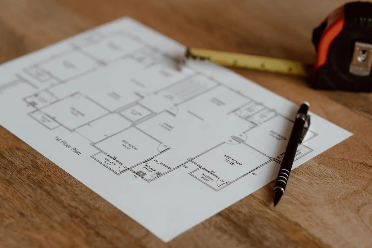 Bản vẽ mặt bằng căn nhà trên giấy trắng cạnh bút và thước cuộn