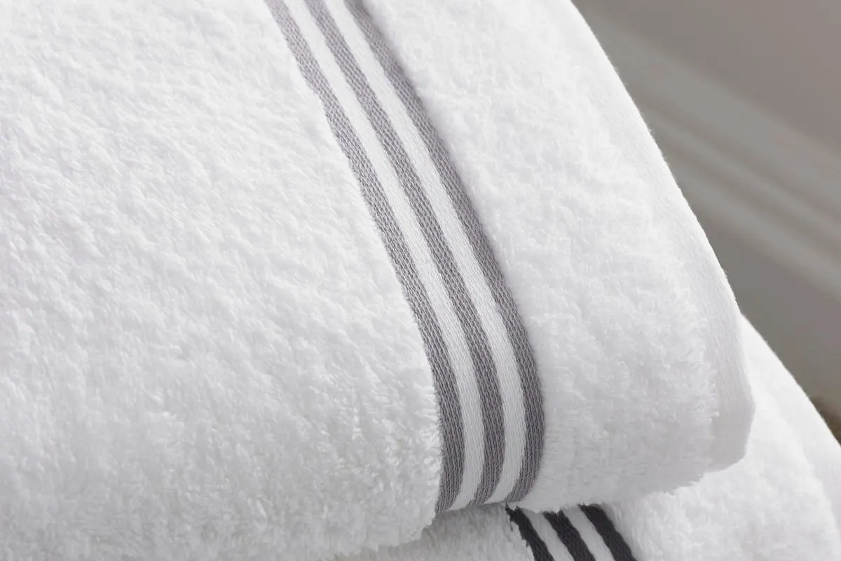 Two stacked white terry bath towels with grey stripe borders