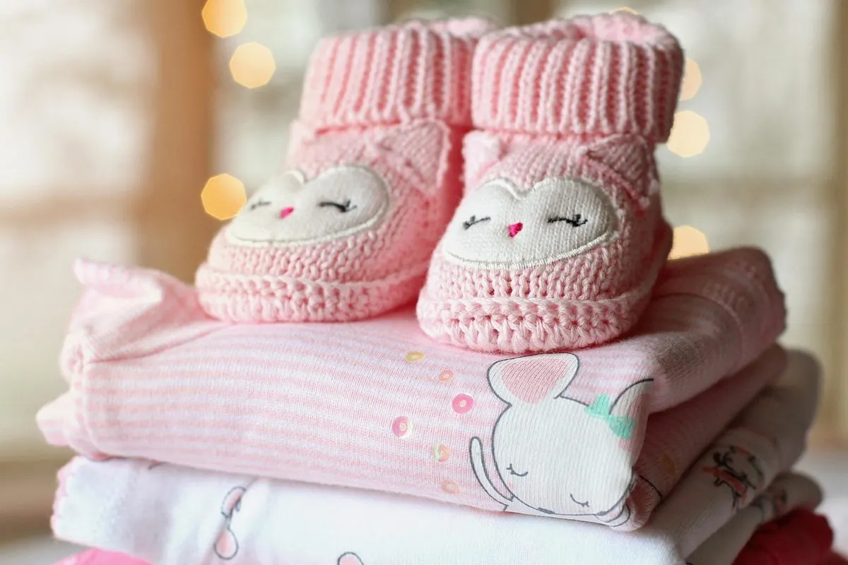 Đôi giày len hồng em bé đặt trên chồng quần áo trẻ em hồng