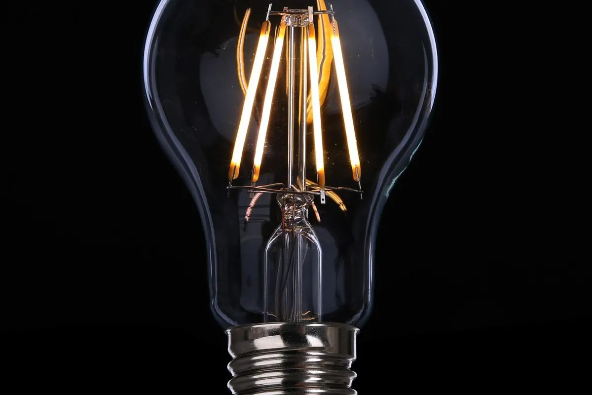 Clear glass light bulb with a glowing filament on a black background