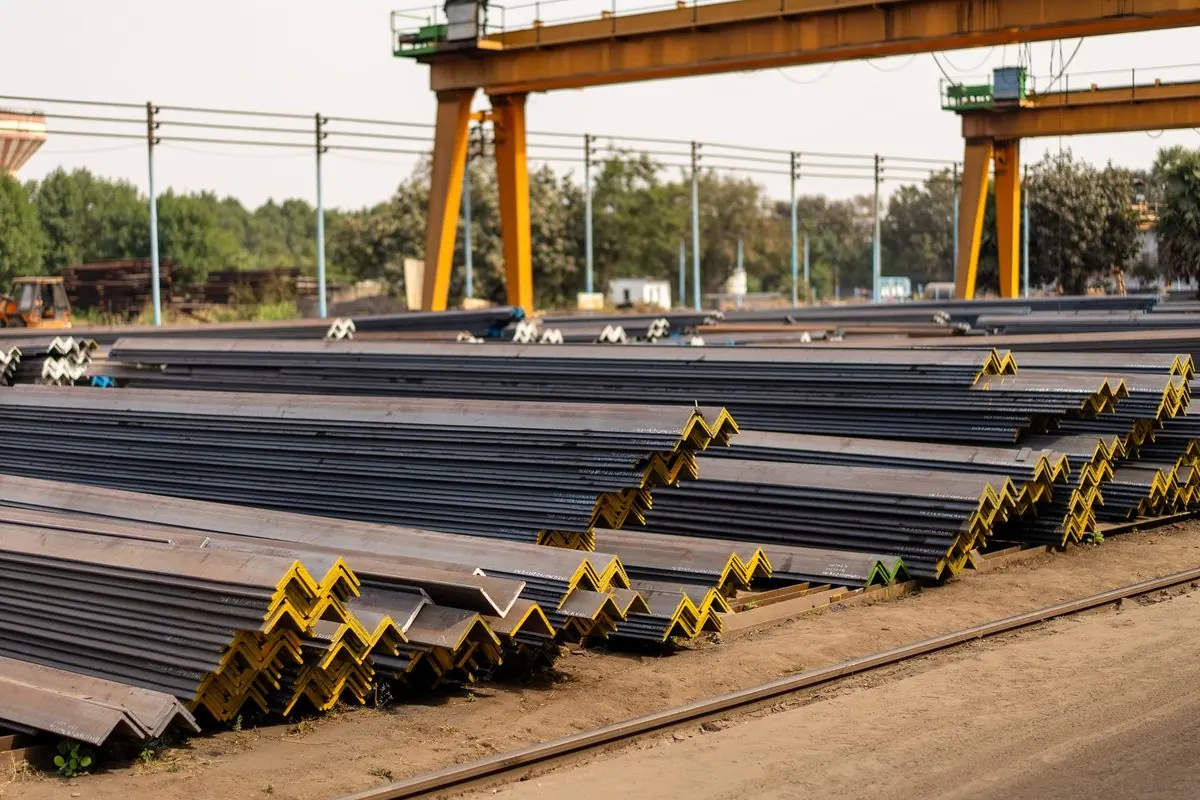 Stacks of steel angles in a yard under a gantry crane