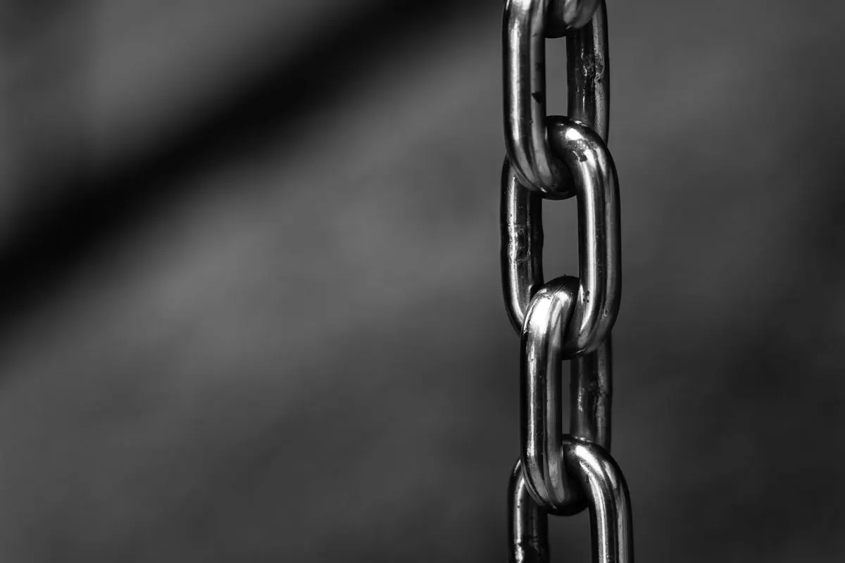 Steel link chain hanging vertically against a blurred grey background