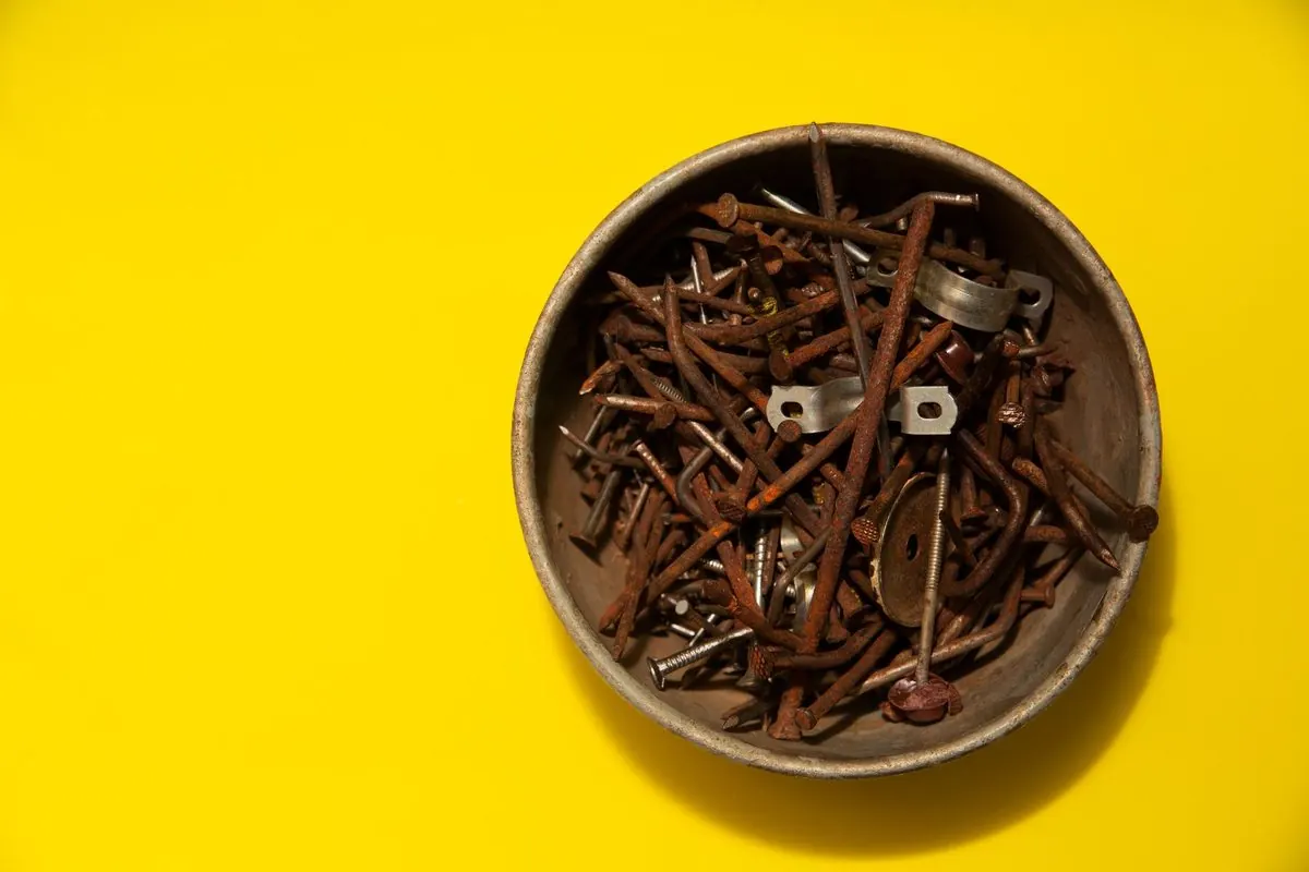 Rusty steel nails in a round tin on a yellow background