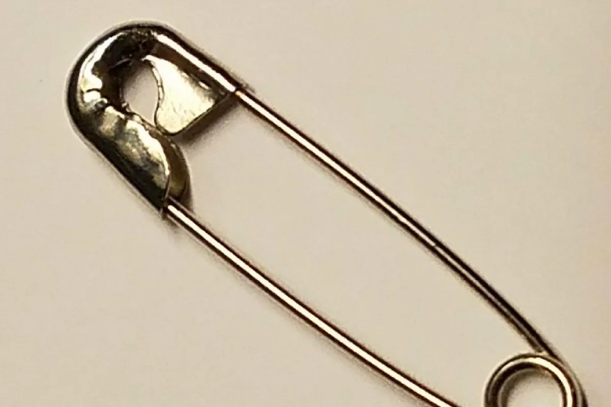 Bright steel safety pin on a beige background