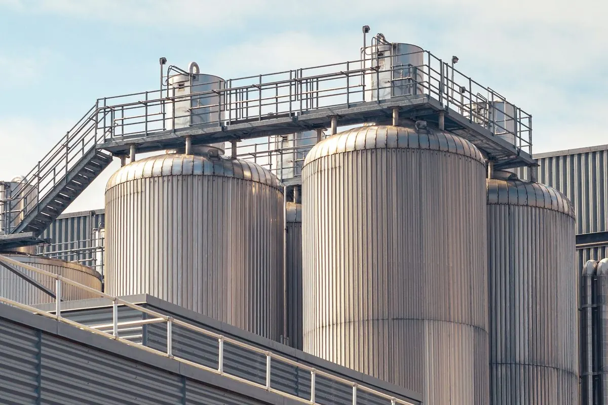 Large cylindrical metal storage tanks with railings and stairs at a plant