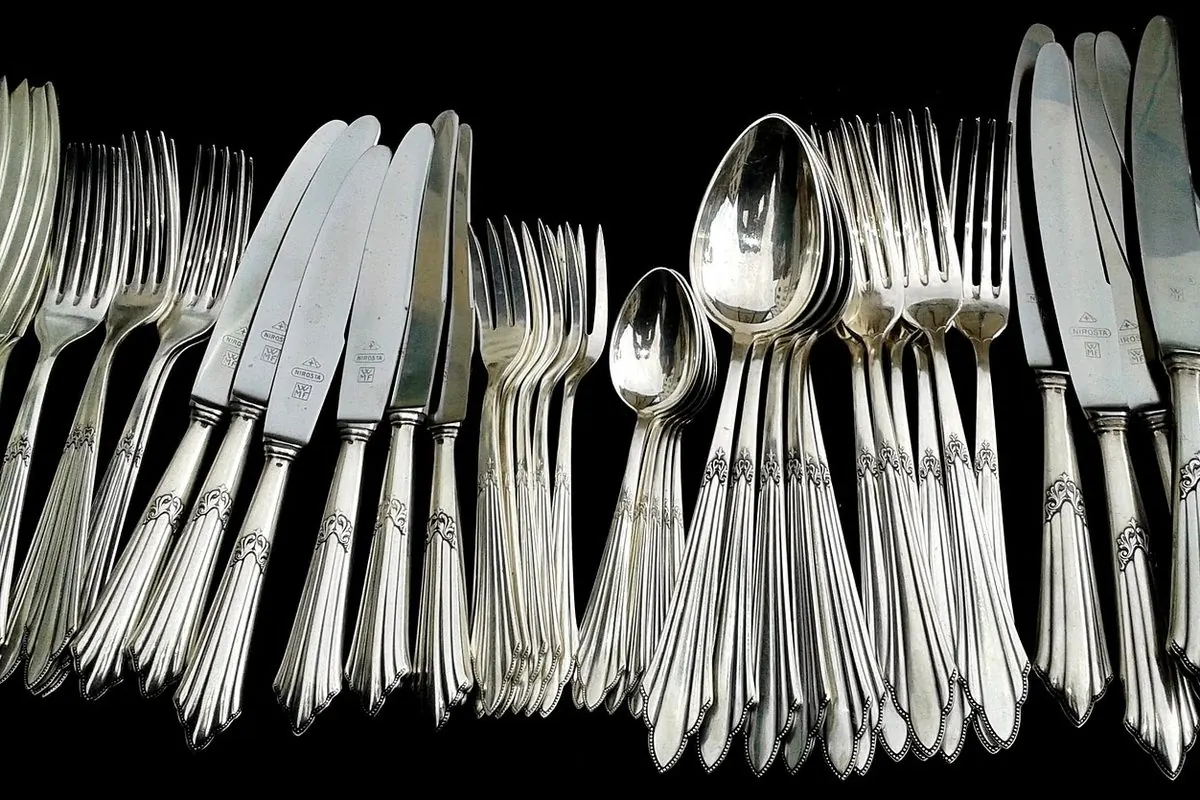 Bộ thìa, dĩa, dao bằng bạc xếp thành hàng trên nền đen