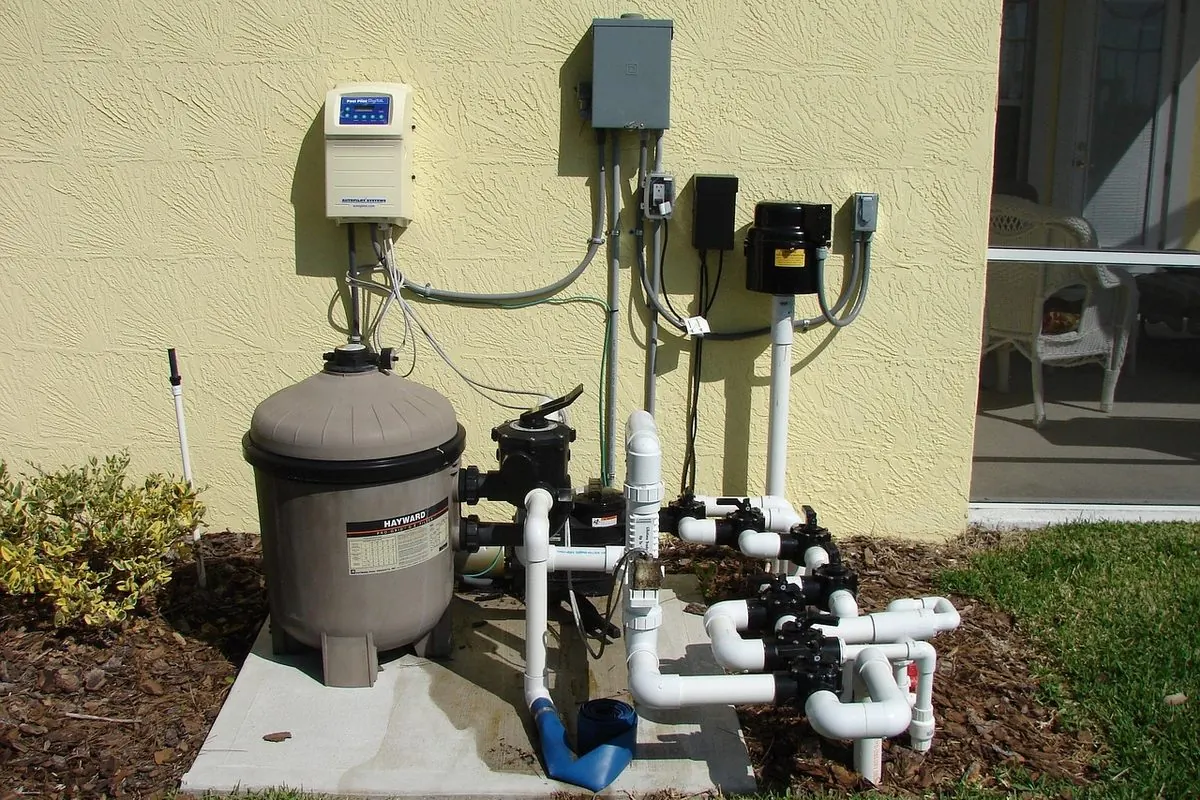 Water filter tank and pump connected to white pipes beside a house wall