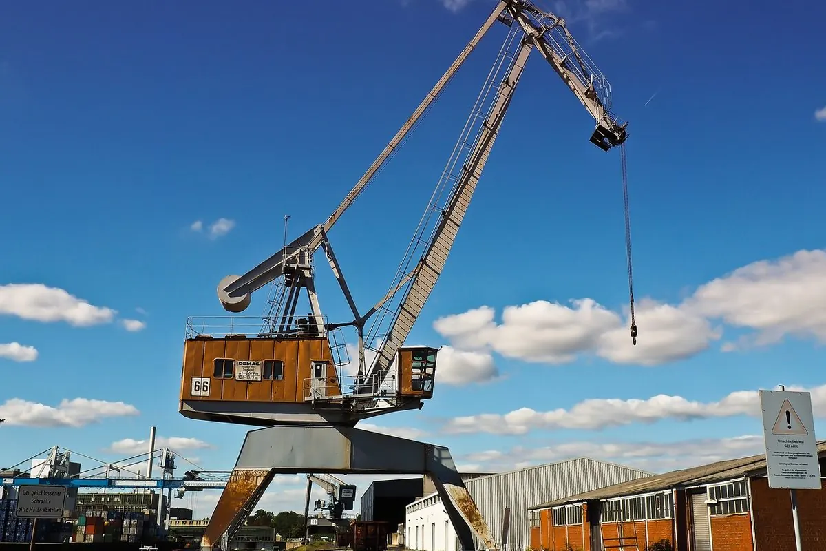 Old harbour jib crane with a long boom beside a warehouse