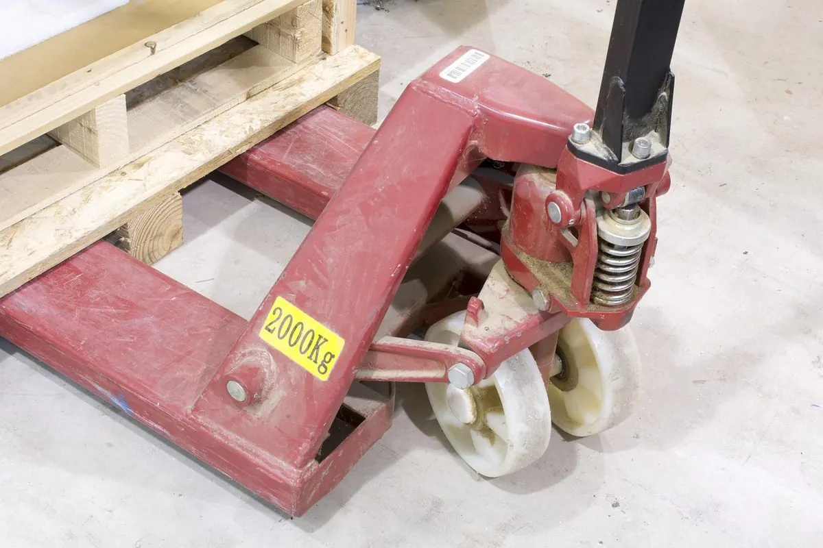 Xe nâng pallet thủ công màu đỏ cạnh pallet gỗ trong kho
