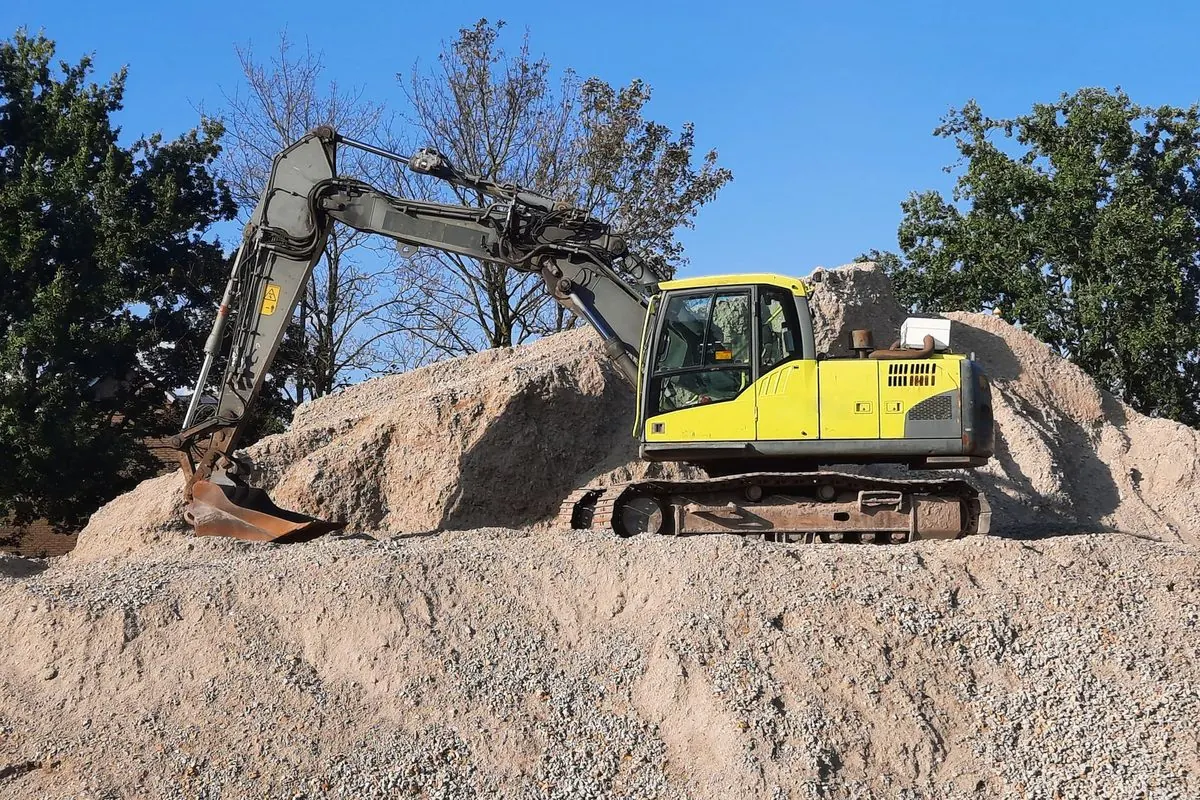 Yellow tracked excavator on a sand pile under a blue sky