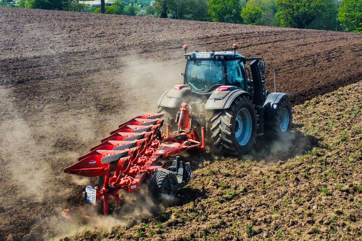 Tractor pulling a red multi-share plough
