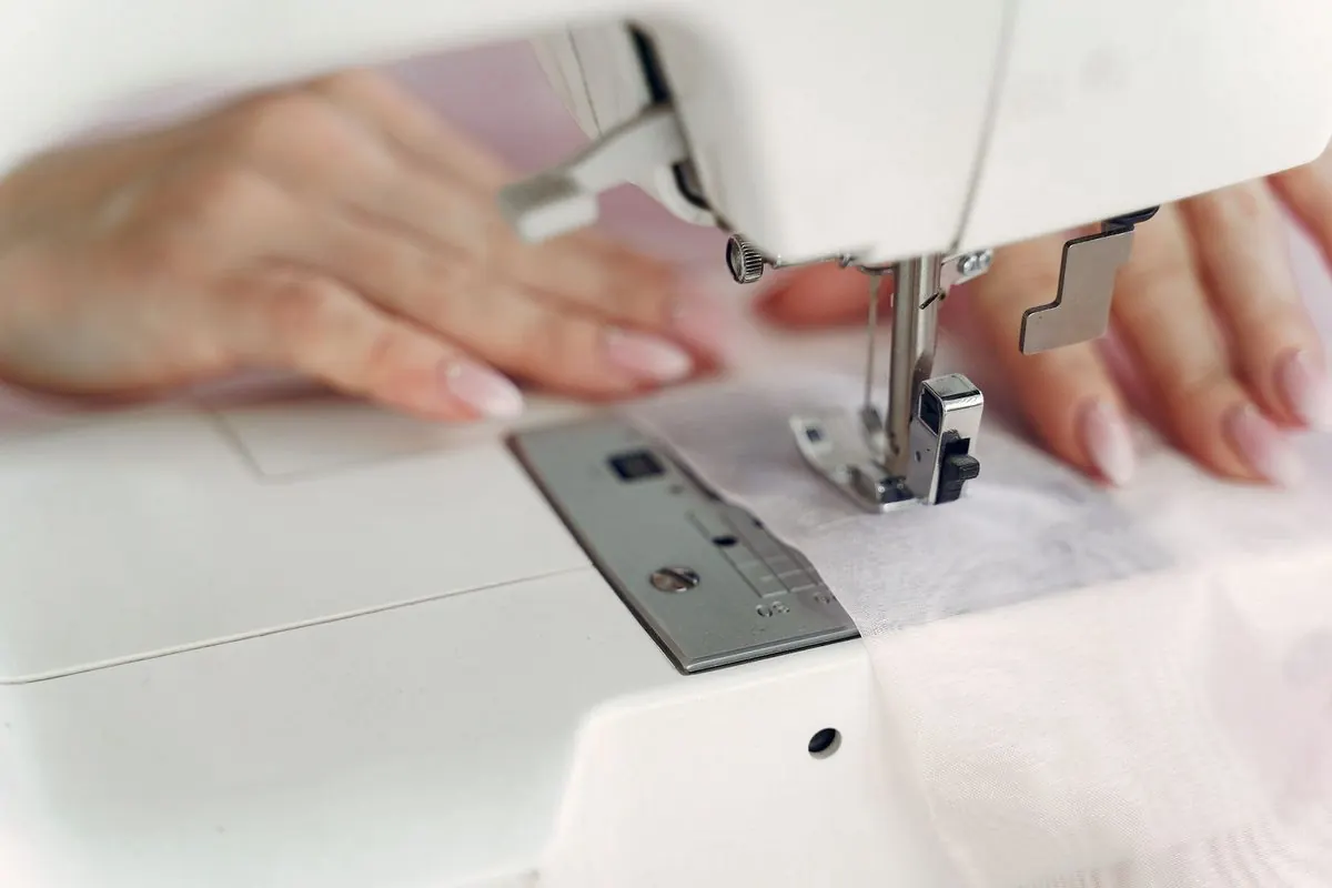 White household sewing machine with hands feeding fabric