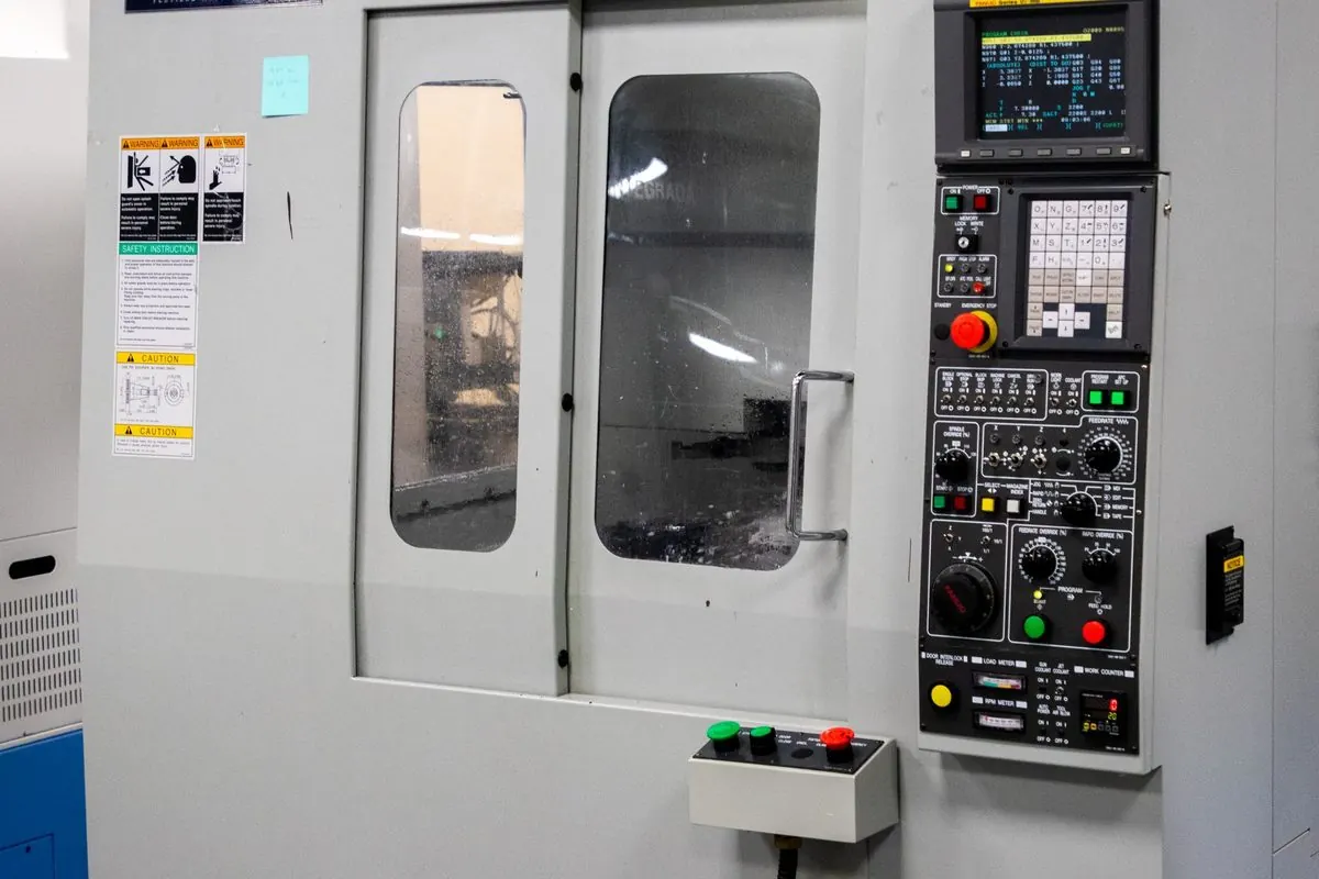 Trung tâm gia công CNC màu trắng xám có cửa kính và bảng điều khiển