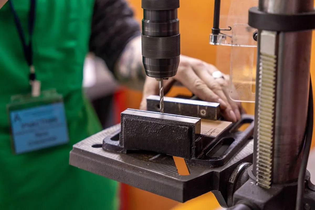 Drill press drilling a metal part clamped in a vise