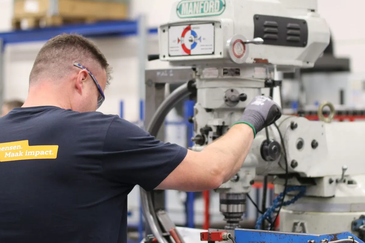 Worker operating a white universal milling machine in a machine shop