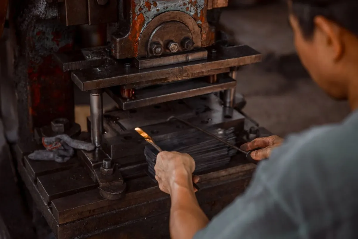 Worker placing a metal blank into a punch press in a workshop