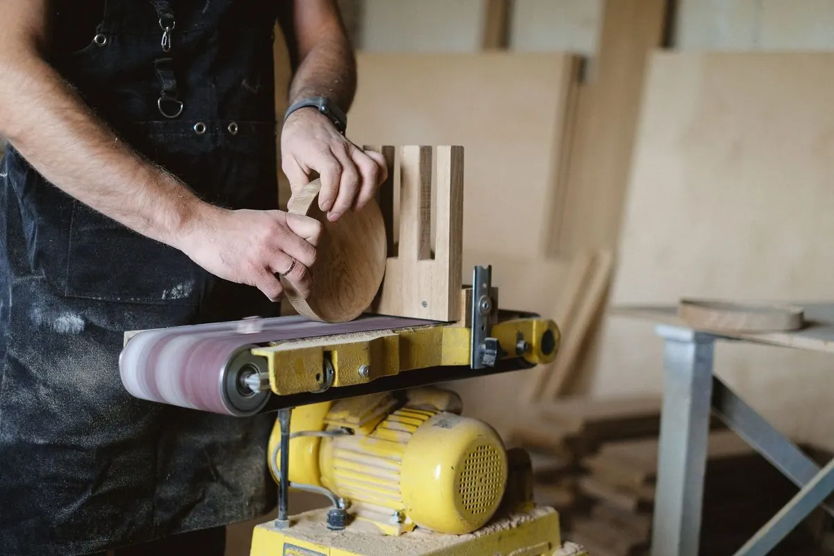 Carpenter sanding a piece of wood on a yellow belt sander