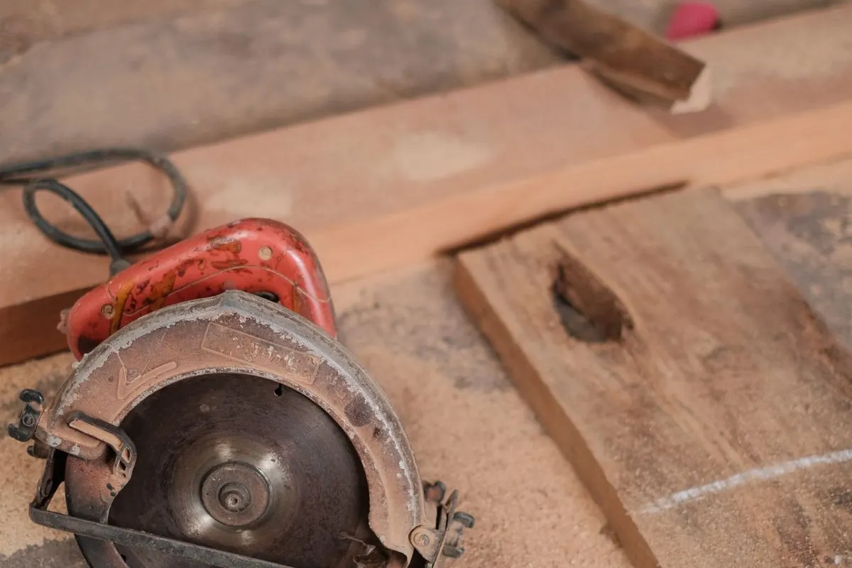 Handheld electric circular saw on a workshop floor beside wood boards