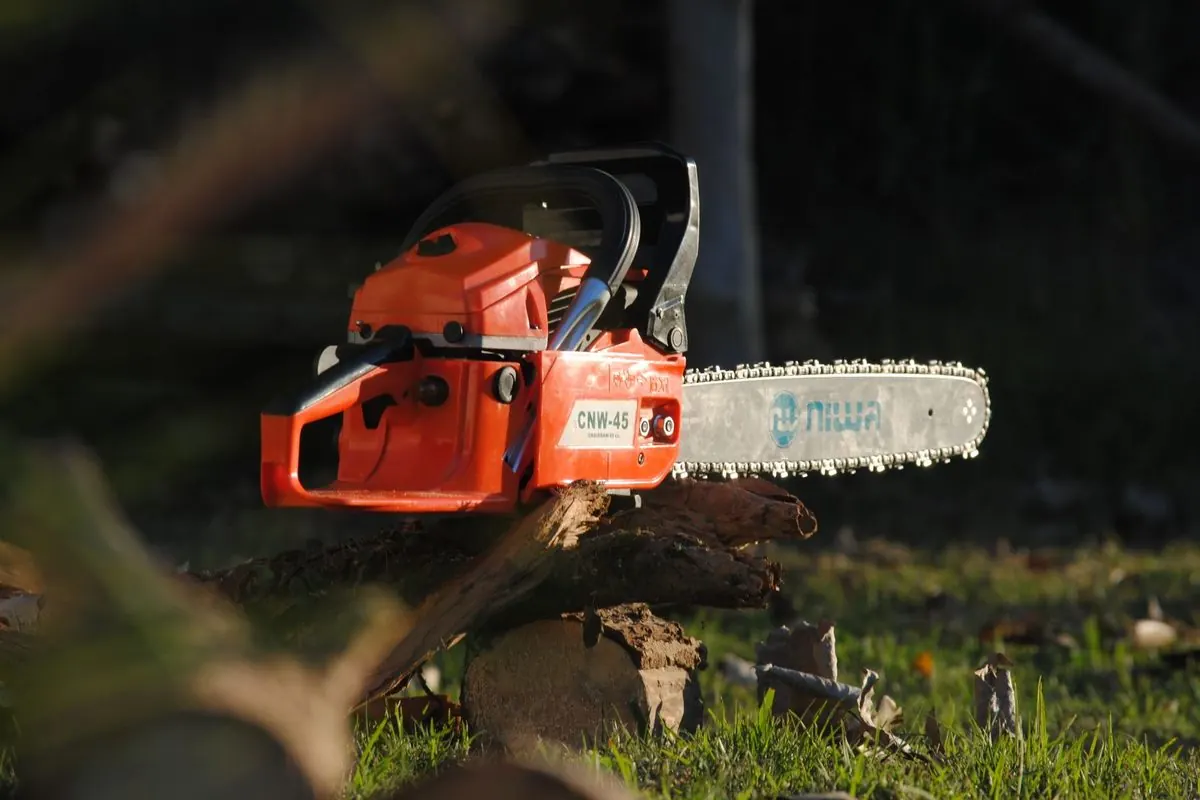 Orange chainsaw resting on a tree log outdoors