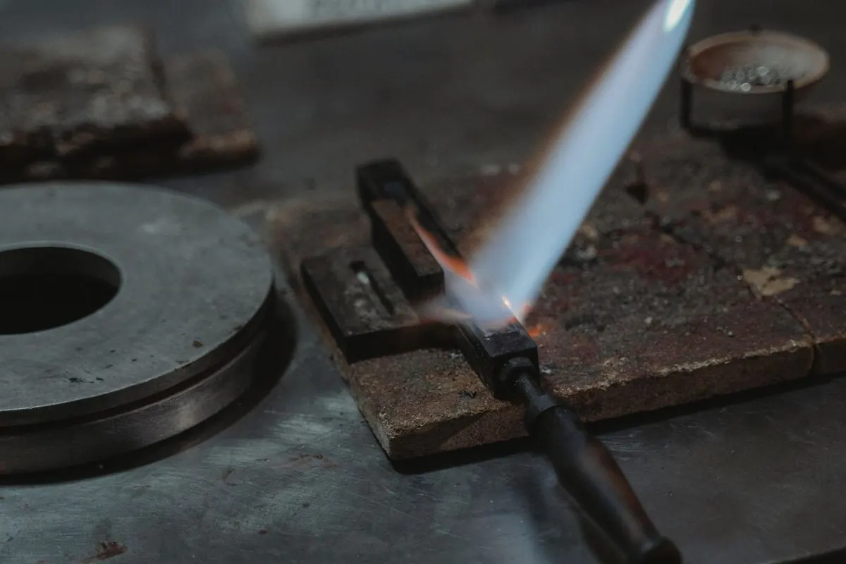 Handheld blowtorch directing a blue flame at a metal mould
