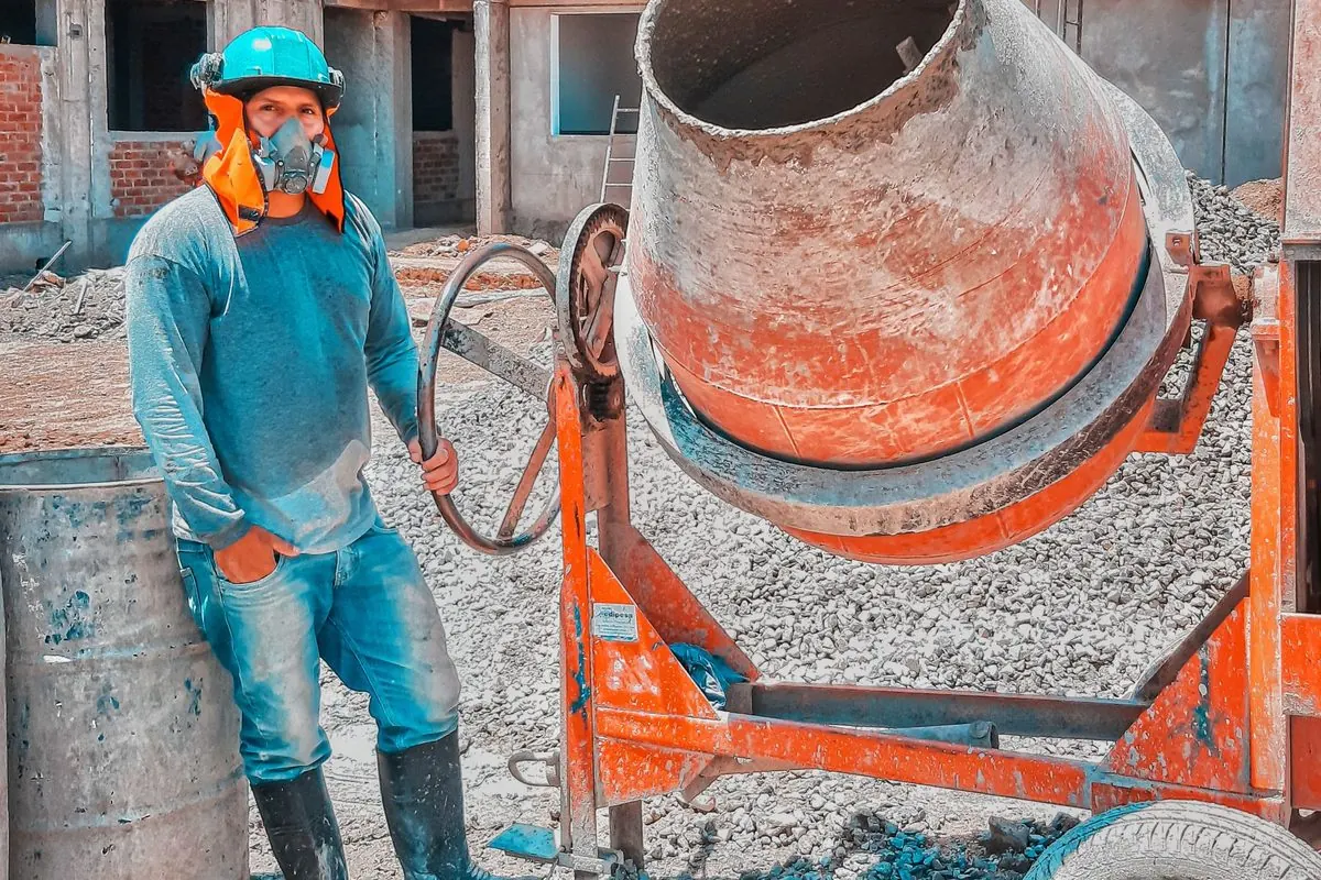 Worker standing beside an orange drum concrete mixer