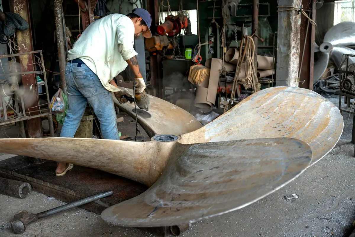 Worker grinding a bronze ship propeller in a workshop