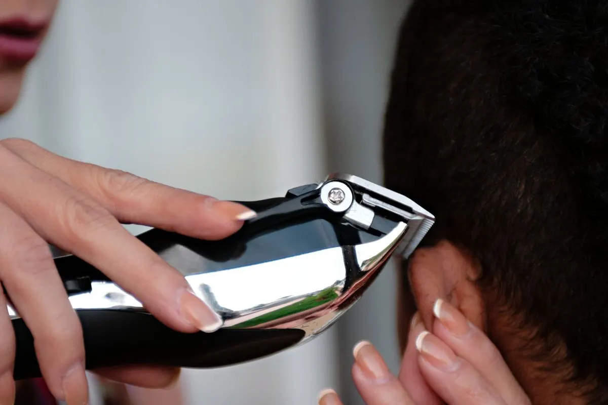 Hand holding a silver electric hair clipper at a client's neck